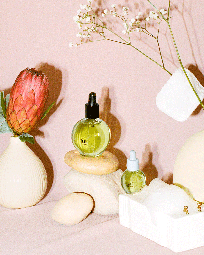 Fur Oil and Ingrown Concentrate on top of pink rocks next to a flowers against a pink background.